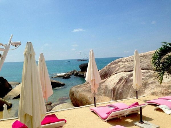 Pink-cushioned loungers and closed umbrellas beside coastal boulders at Beluga Boutique Hotel
