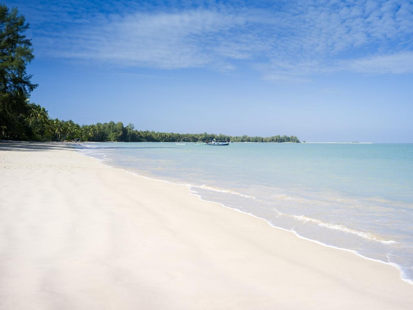 Sandy beach with pale blue sea and boats offshore at The Sarojin
